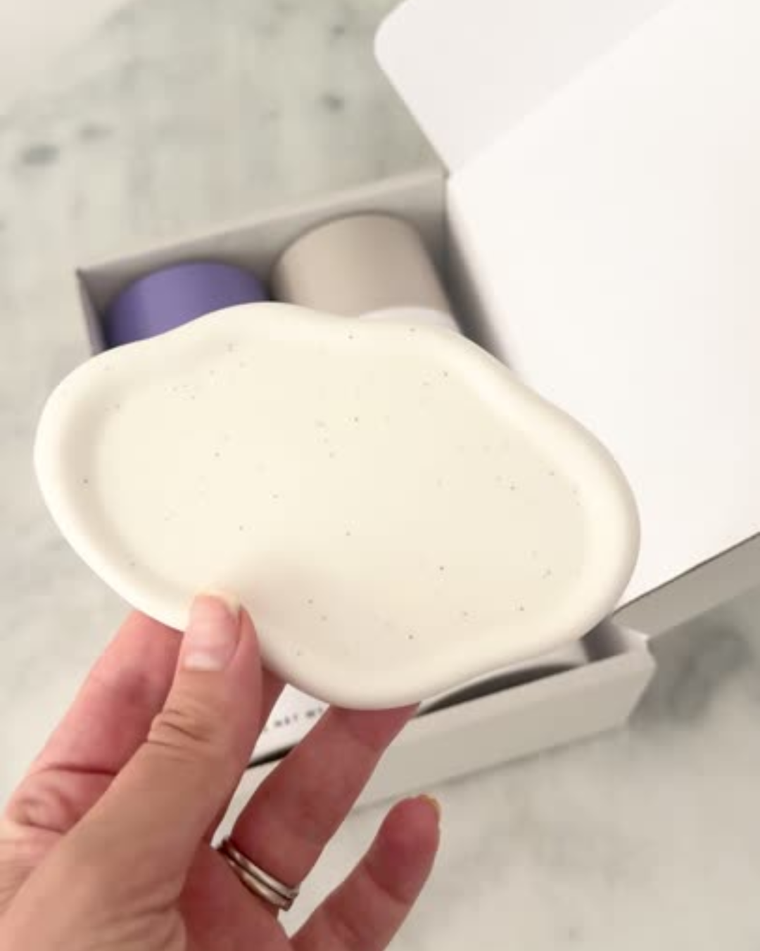 Hand hold an essential oil shower steamer dish tray with a blurred background of essential oil shower steamer canisters