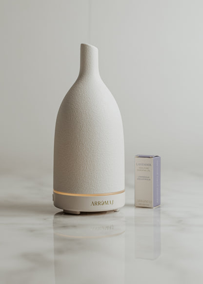 A white ceramic essential oil ultrasonic diffuser with a small box of lavender essential oils in front, placed on a marble surface.
