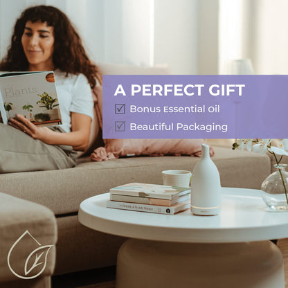 a lady reading a book on a couch with a ceramic essential oil diffuser being used on a coffee table. text overlay saying perfect gift, bonus essential oil, beautiful packaging